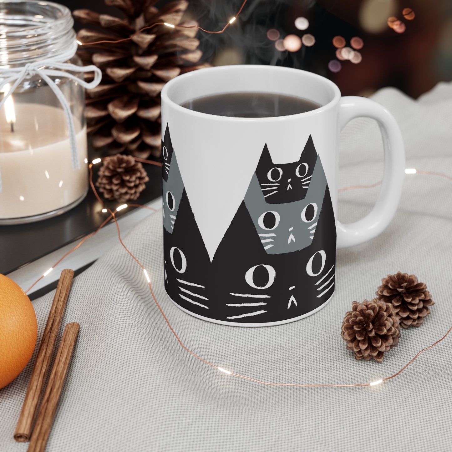 Ceramic mug featuring a pattern of black and gray cat faces with wide eyes, modern minimalist cat illustration