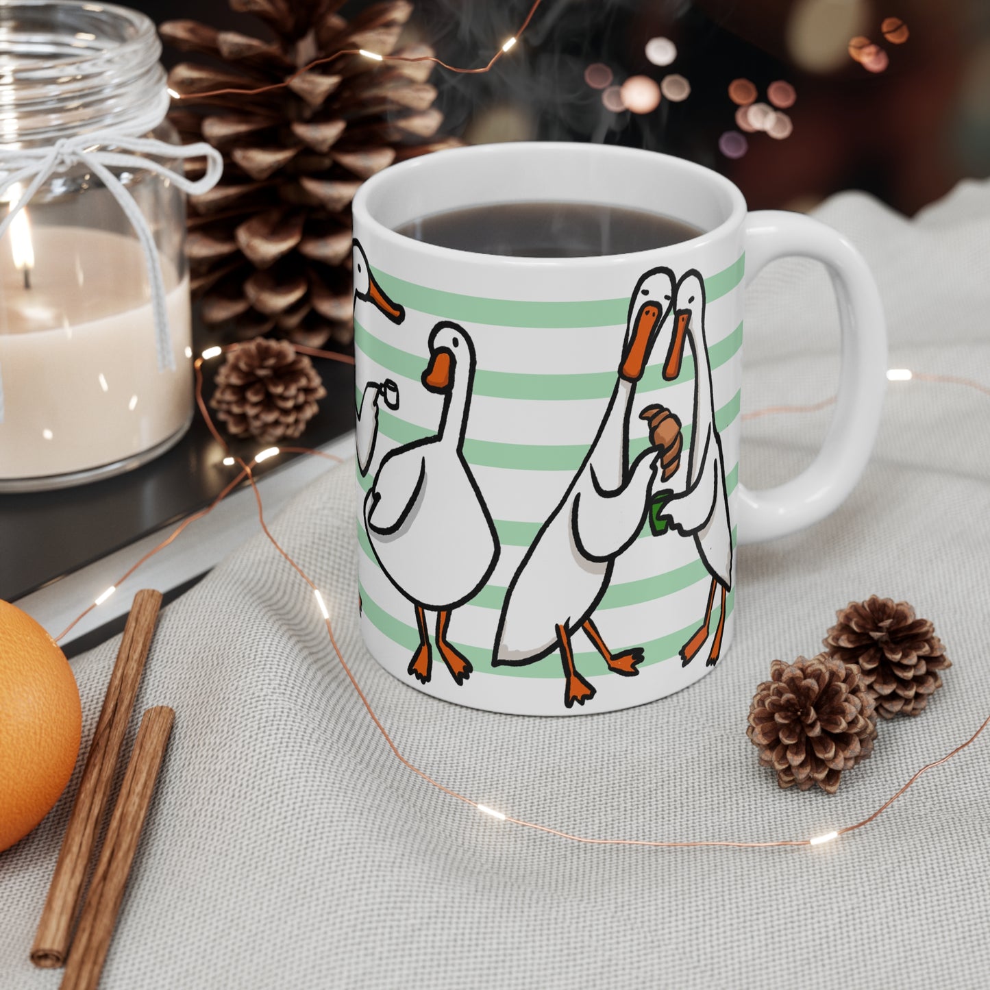 White ceramic mug featuring illustrated ducks drinking coffee, holding mugs, and sharing croissants on a green striped background.