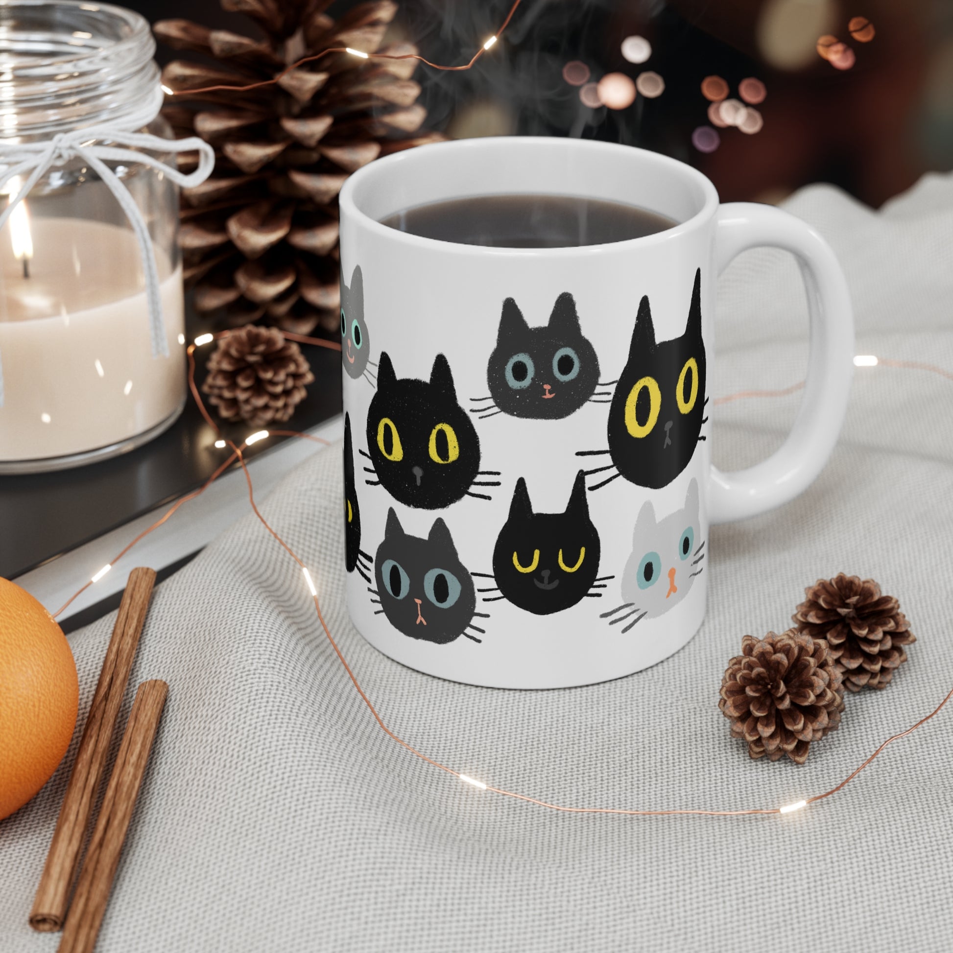 Ceramic mug featuring rows of illustrated cat faces in black, gray, and white tones with playful, wide-eyed expressions.