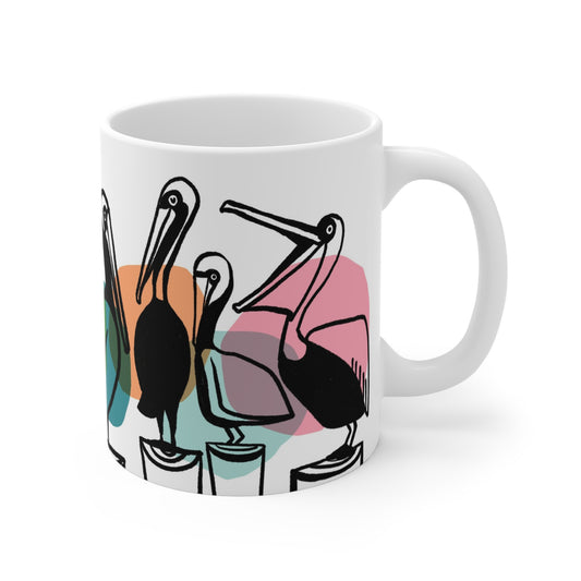 White ceramic mug featuring illustrated pelicans lined up on pilings with colorful abstract shapes behind them