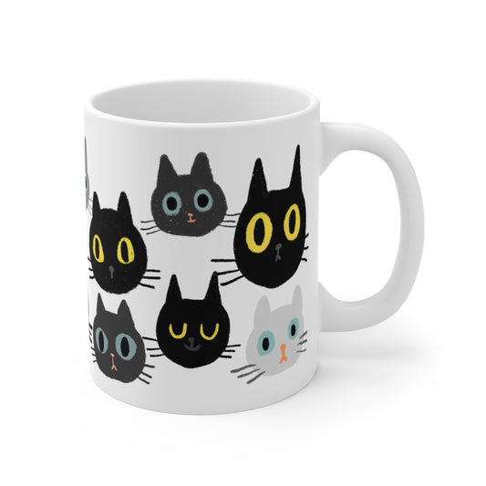 Ceramic mug featuring rows of illustrated cat faces in black, gray, and white tones with playful, wide-eyed expressions.