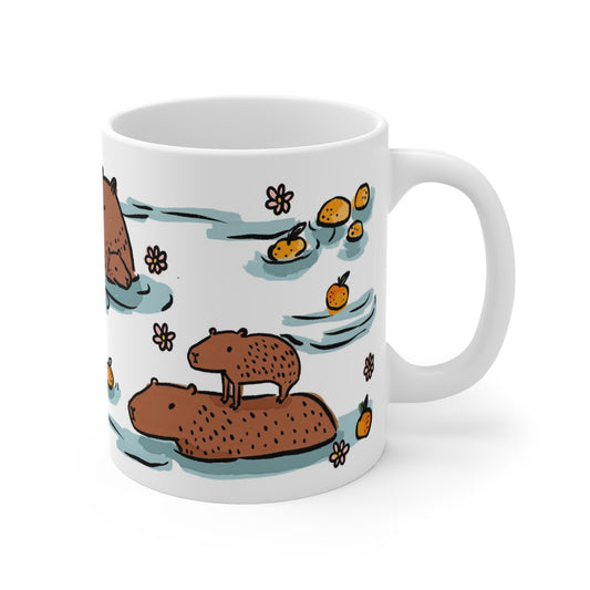 White ceramic mug featuring illustrated capybaras relaxing in a warm bath surrounded by floating oranges and flowers.