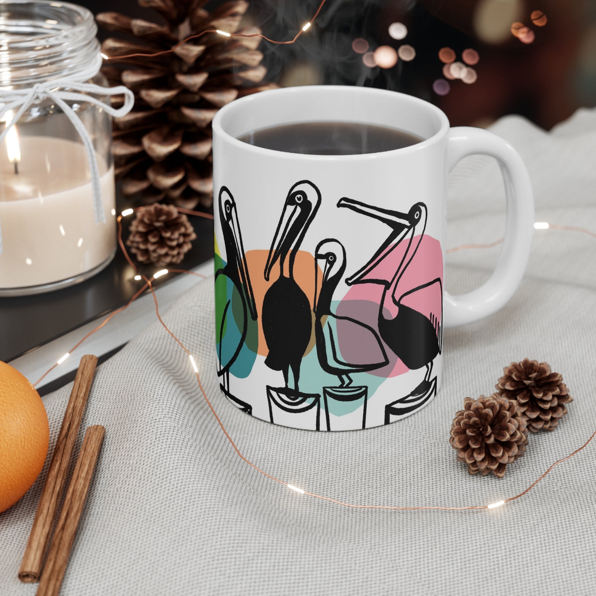 White ceramic mug featuring illustrated pelicans lined up on pilings with colorful abstract shapes behind them