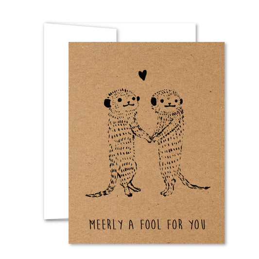 Greeting card with two hand-drawn meerkats holding paws under a heart, black line art on kraft background—perfect for love or friendship.