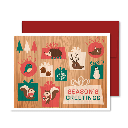 Woodland animals in festive gift boxes and ornaments on wood background, “Season’s Greetings” holiday greeting card